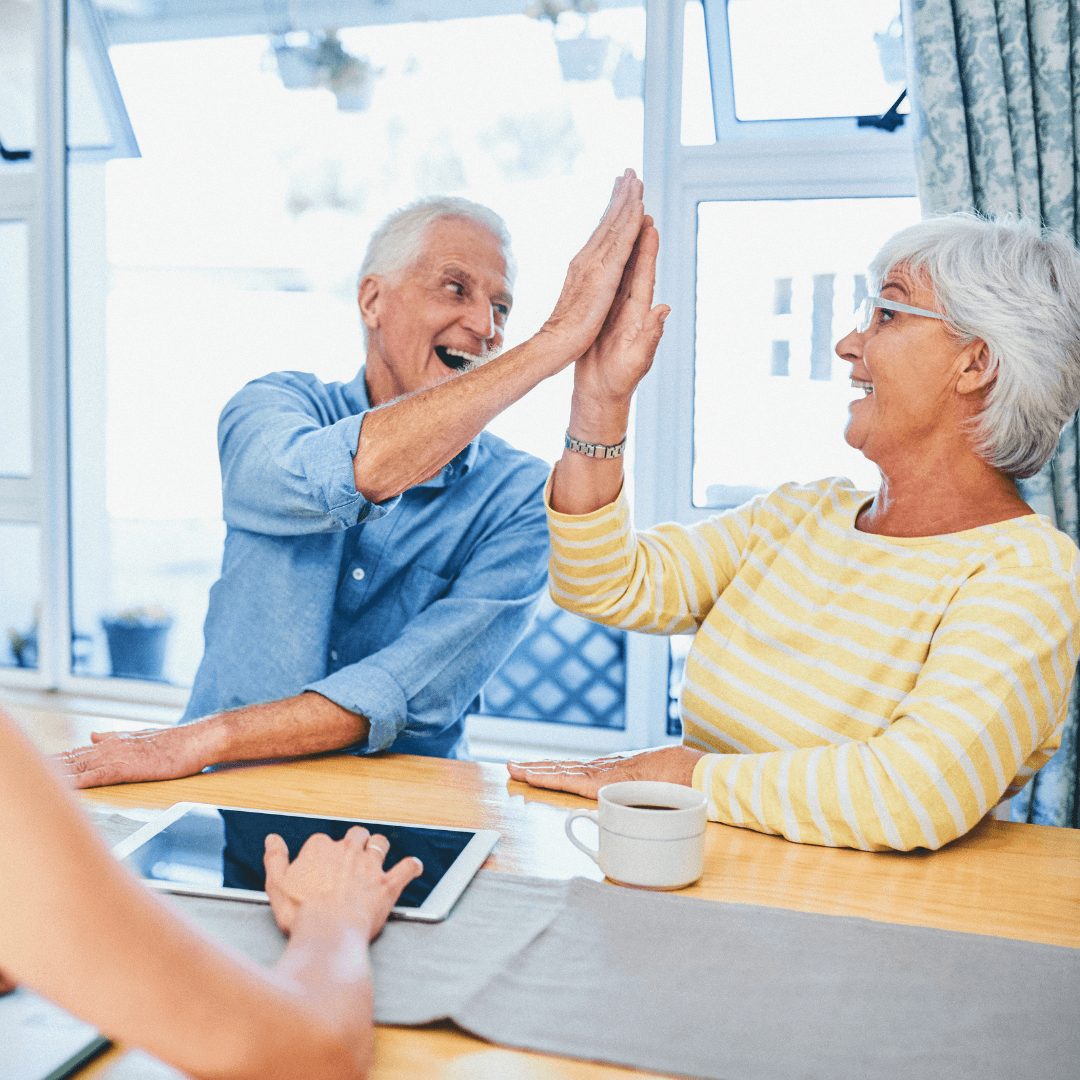 An elderly couple enthusiastically slap hands, expressing their joy and complicity.