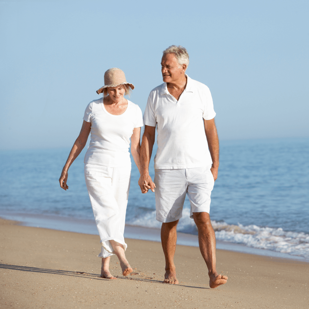 A couple dressed all in white stroll along a beach