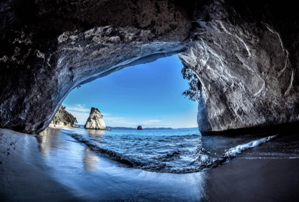 View from inside a seaside cave, with waves and rocks in the background, creating a tranquil atmosphere.