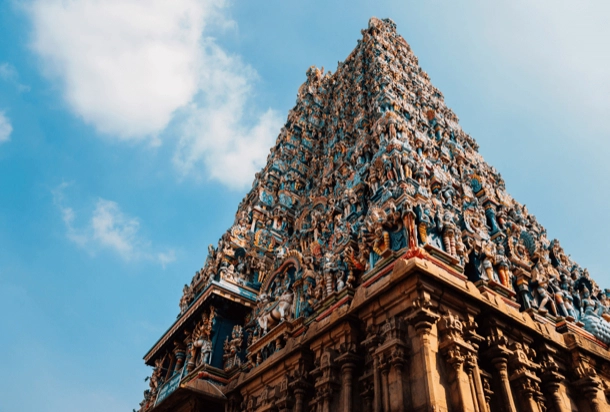 The image shows a detailed view of an intricately carved temple tower against a clear blue sky, highlighting the rich cultural artistry and architectural significance. The temple’s vibrant colors and elaborate sculptures make it an interesting subject representing historical and religious importance. 