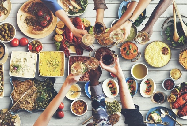 A lively gathering at a table filled with various foods and drinks, as people raise their glasses in a toast.