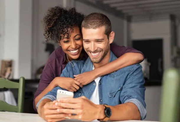 A smiling man and woman looking at their phone together.