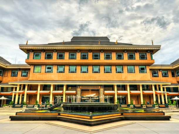 The image shows a large, traditional building with a tiered roof and orange walls, situated behind a decorative fountain. The architecture suggests cultural significance or institutional importance, making it an interesting subject for its design and function. 