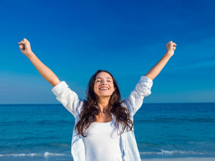 woman smiling with arms in the air and the sea as background