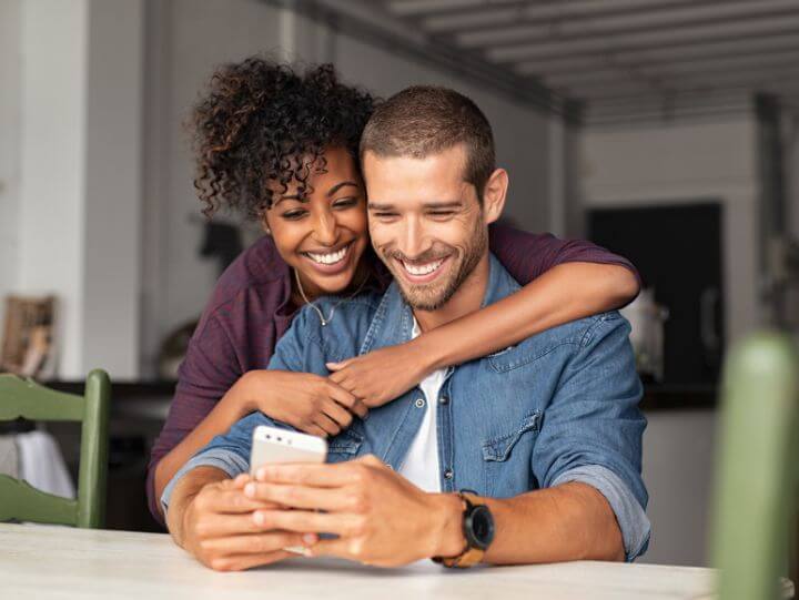 A smiling man and woman looking at their phone together.