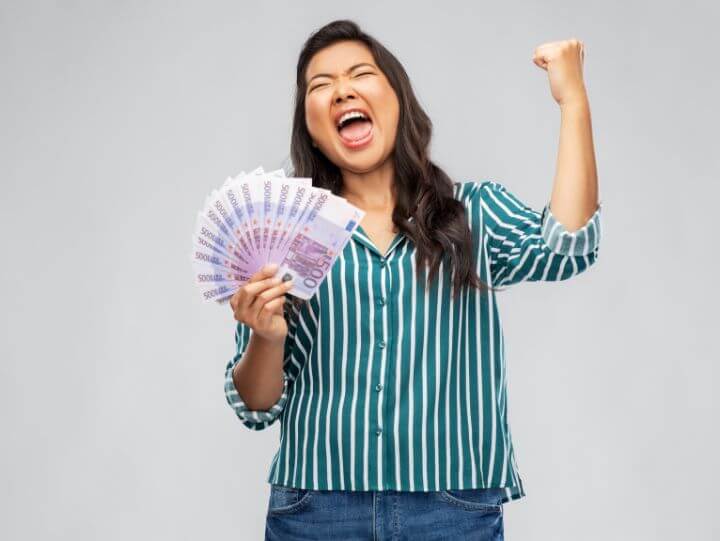 A woman smiling and raising cash in celebration.