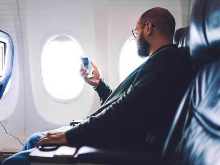 A man sitting in an airplane seat, using his cell phone.