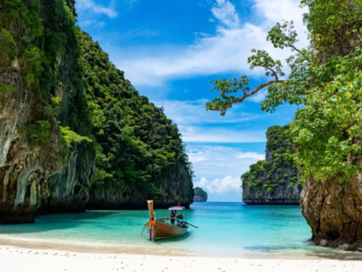 Boat docked on sandy beach near towering cliff.